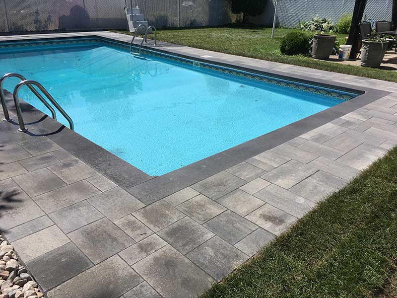 Pavers around a pool. Black borders with dark grey.